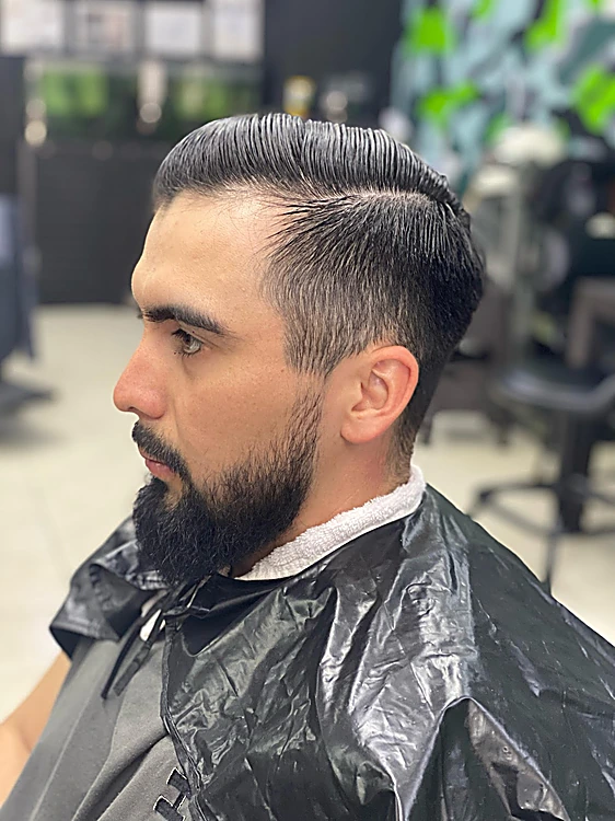 Pompadour peinado hacia atrás con degradado en los lados y barba completa perfilada, de perfil
